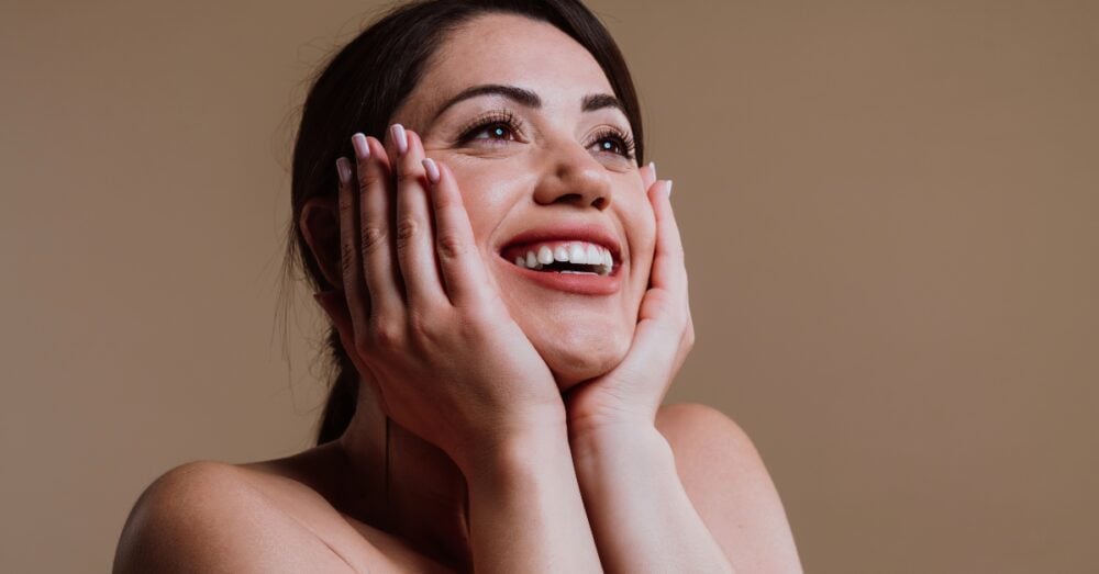Woman with glowing skin smiling and touching her face
