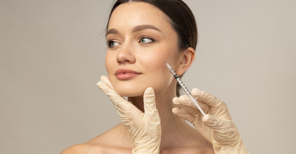 A young woman looking to the side while a gloved provider prepares to perform masseter Botox for facial slimming