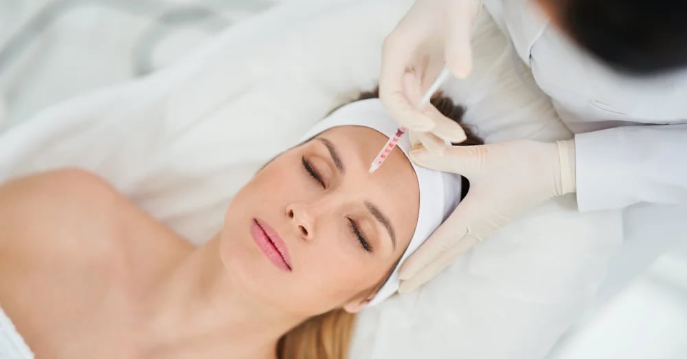 A woman with closed eyes lying back in a reclined position while a gloved hand administers an injection