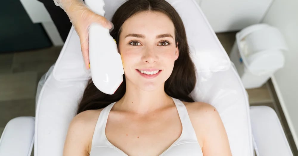 A smiling young woman lying on a treatment bed receiving an IPL photofacial session