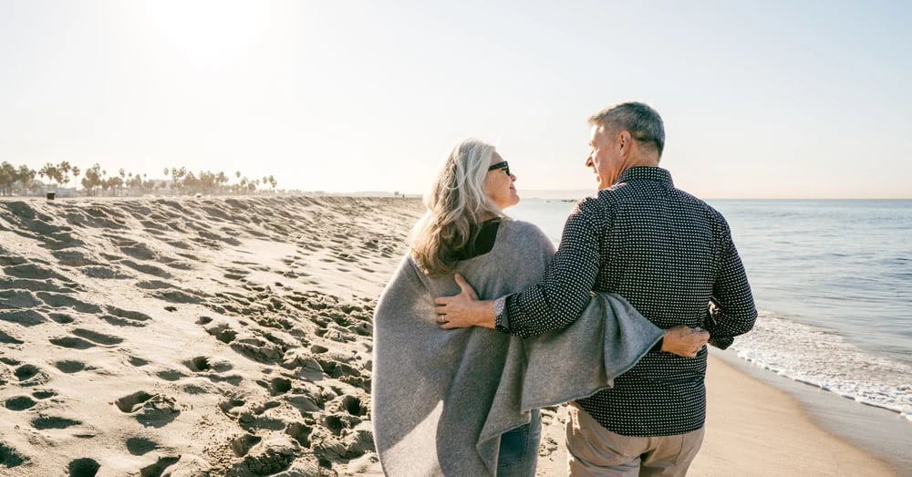 A couple walking along the shoreline of a beach with their arms around each other