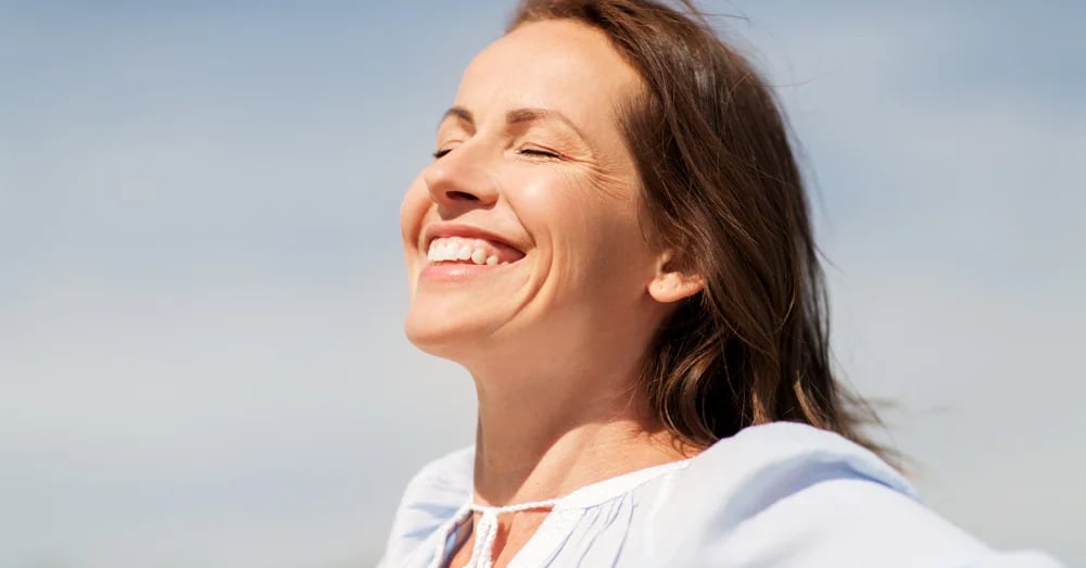 Woman smiling with her eyes closed against a blue background