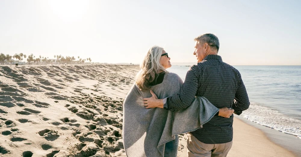A couple with their arms aroun each other, walking along the shoreline of a beach