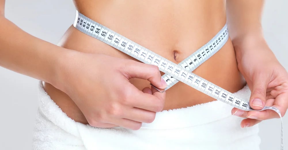 Close-up of a woman measuring her waistline using a measuring tape
