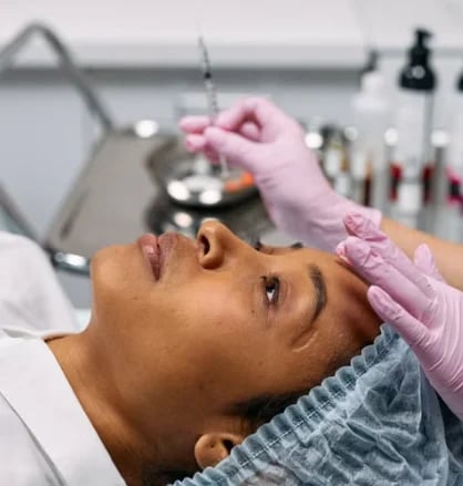 Gloved provider steadying a patient’s brow before a forehead injection