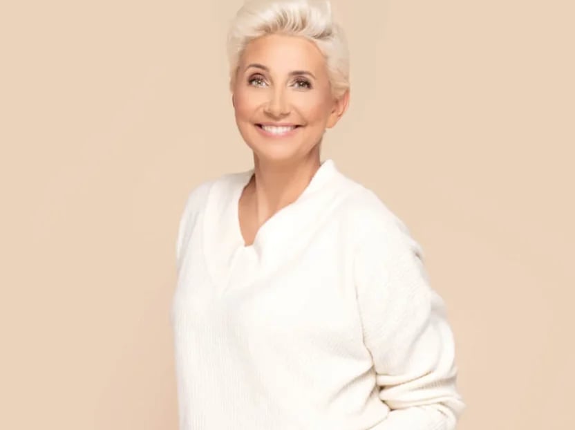 Smiling woman with short platinum hair in a cream sweater against a beige backdrop