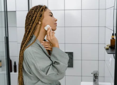 Woman applying skincare with a cotton pad at a bathroom mirror