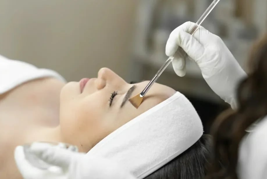 Clinician brushing a peel solution onto the forehead of a patient lying back