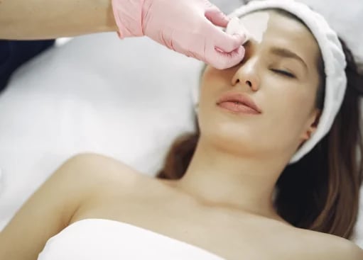Provider cleansing a patient’s forehead with a cotton pad before a facial treatment
